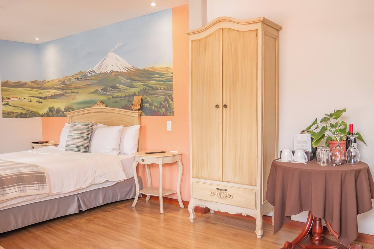 A bedroom with a bed, a nightstand, a wardrobe, a small table with a plant, and a wall mural.