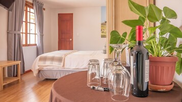 Et hotelværelse med en seng, et bord med vinglas og en flaske vin, samt en potteplante.