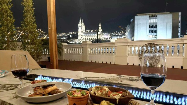 Ein Esstisch mit Speisen und Weingläsern, mit Blick auf eine nächtliche Skyline.