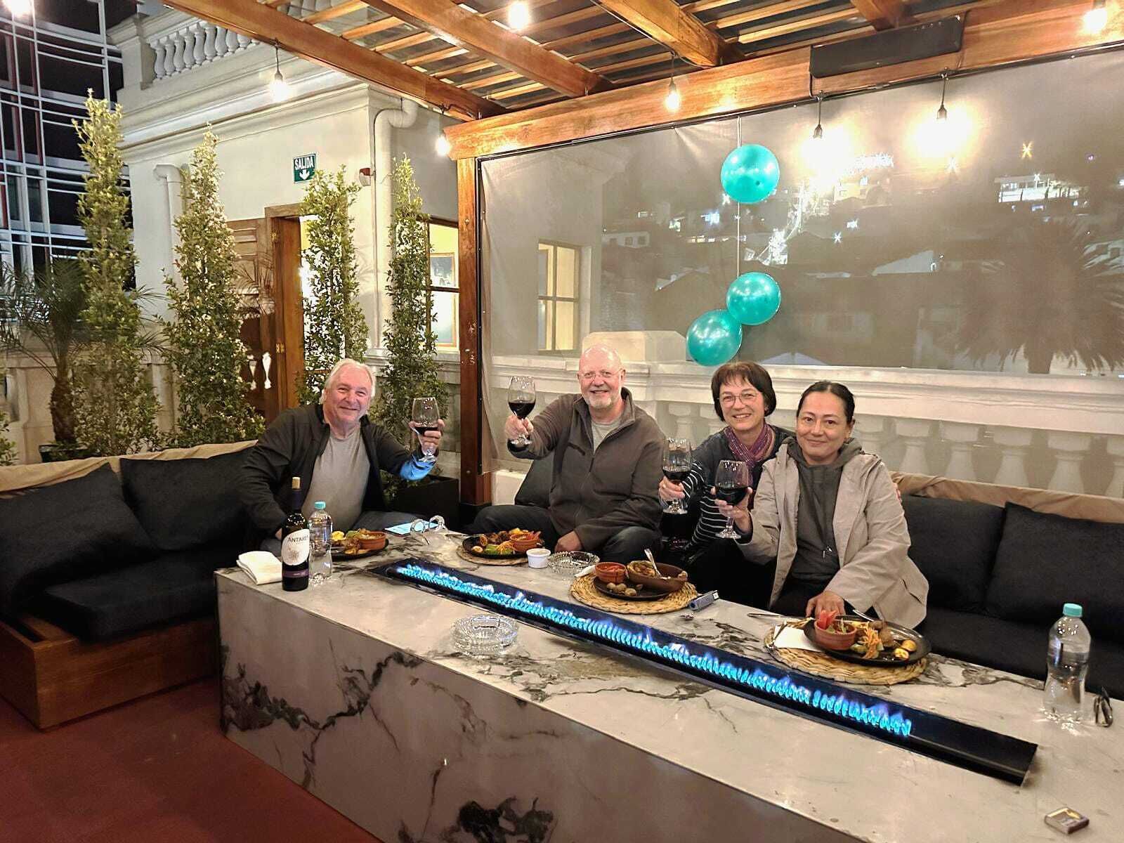 Un groupe de personnes est assis autour d’une table en marbre, où sont disposés de la nourriture et des boissons, dans une pièce dont le plafond est en bois et qui possède de grandes fenêtres.