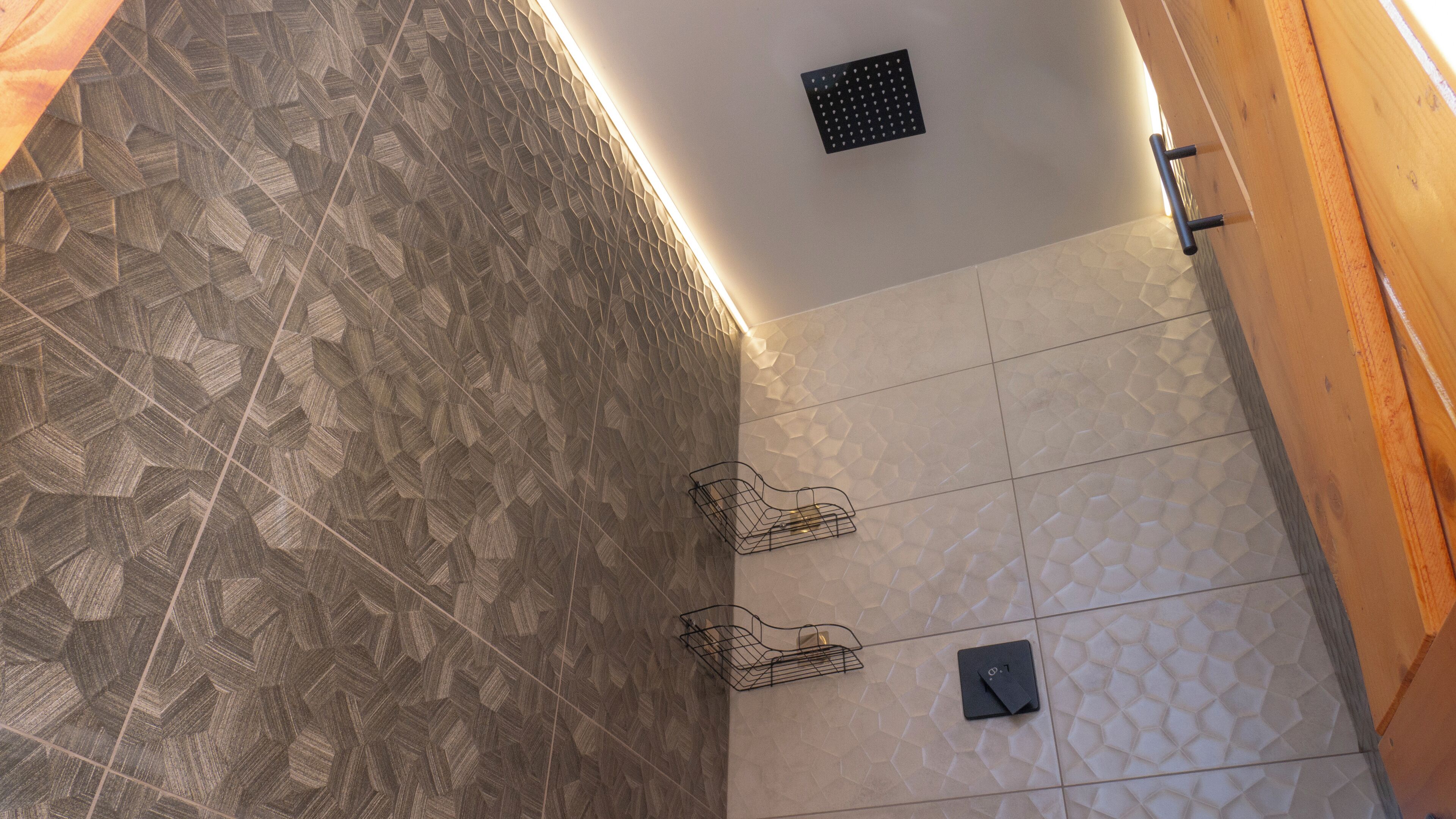 Un coin de pièce aux murs ornés de motifs, une grille de ventilation au plafond et un petit objet noir accroché au mur.