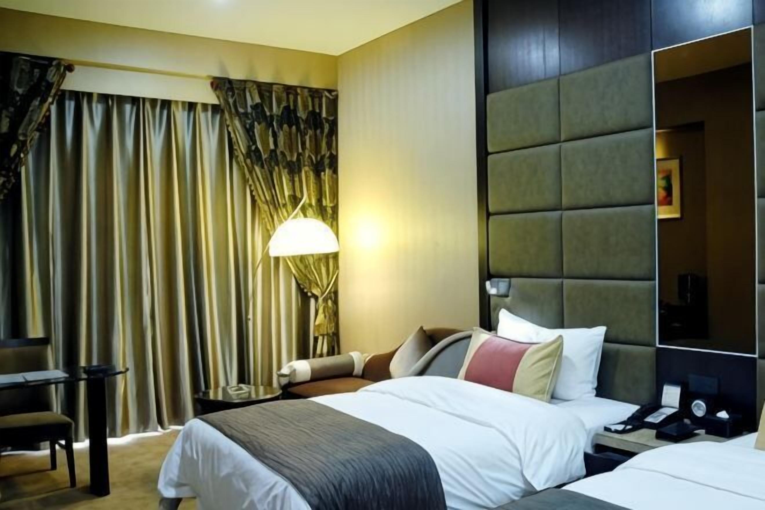 A hotel room with a bed, bedside table, lamp, and a large mirror.