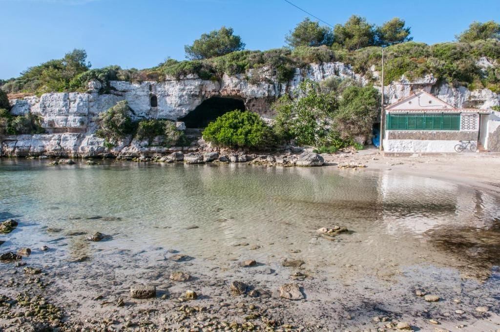 A coastal scene with a rocky shoreline, a cave entrance, and a building with a green door.