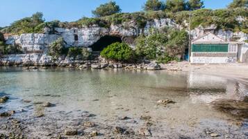A coastal scene with a rocky shoreline, a cave entrance, and a building with a green door.