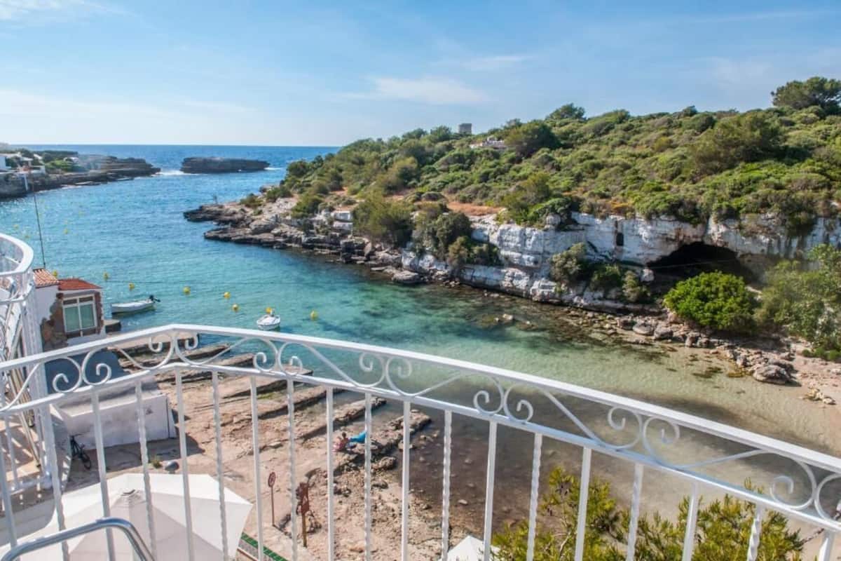 A coastal view from a balcony with clear water, rocky cliffs, and greenery.