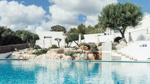 Une piscine à l’eau d’un bleu cristallin, entourée de bâtiments blancs, d’arbres et d’un paysage rocheux.