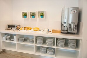 A breakfast bar with a coffee machine, pastries, and stacked plates. - Xuroy (Sant Lluis)
