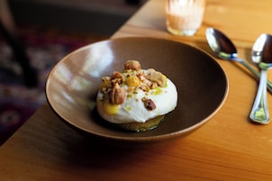 A dessert on a plate with a spoon and a glass in the background.