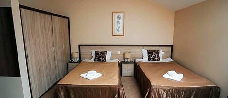 A bedroom with two beds, a wardrobe, a framed picture on the wall, and a small table.