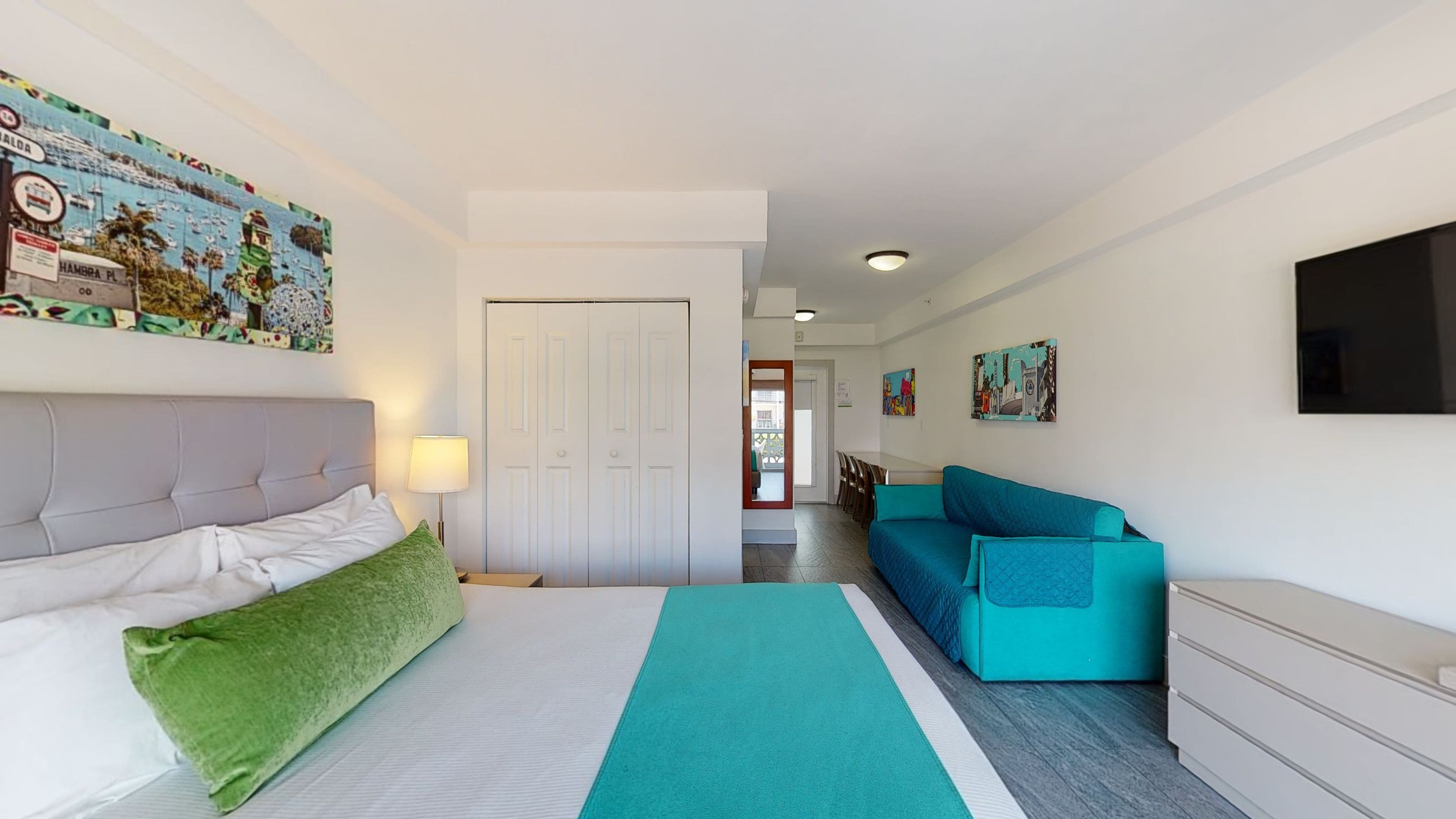 Quarto de hotel com cama, sofá, escrivaninha e porta.