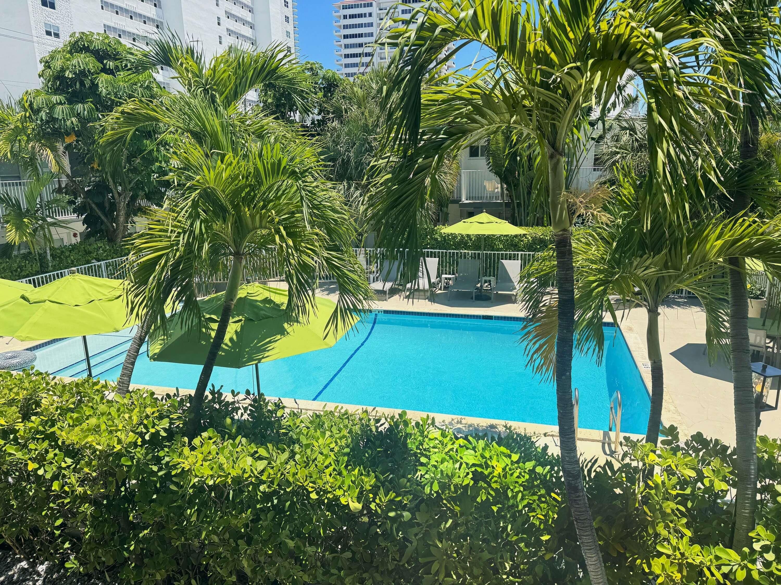 A swimming pool surrounded by lush greenery and palm trees, with a view of tall buildings in the background.