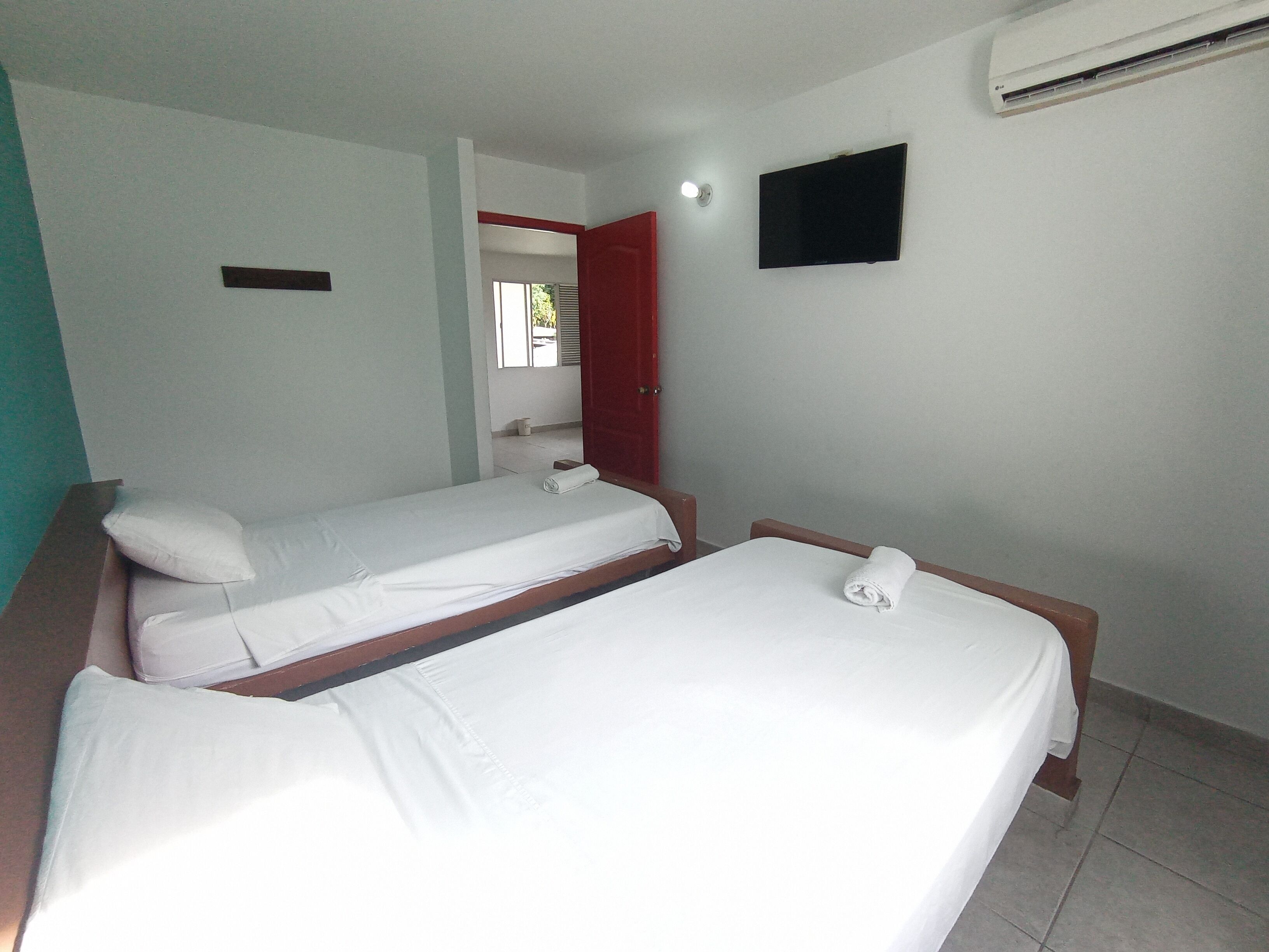 A hotel room with two single beds, a TV mounted on the wall, and an air conditioning unit.