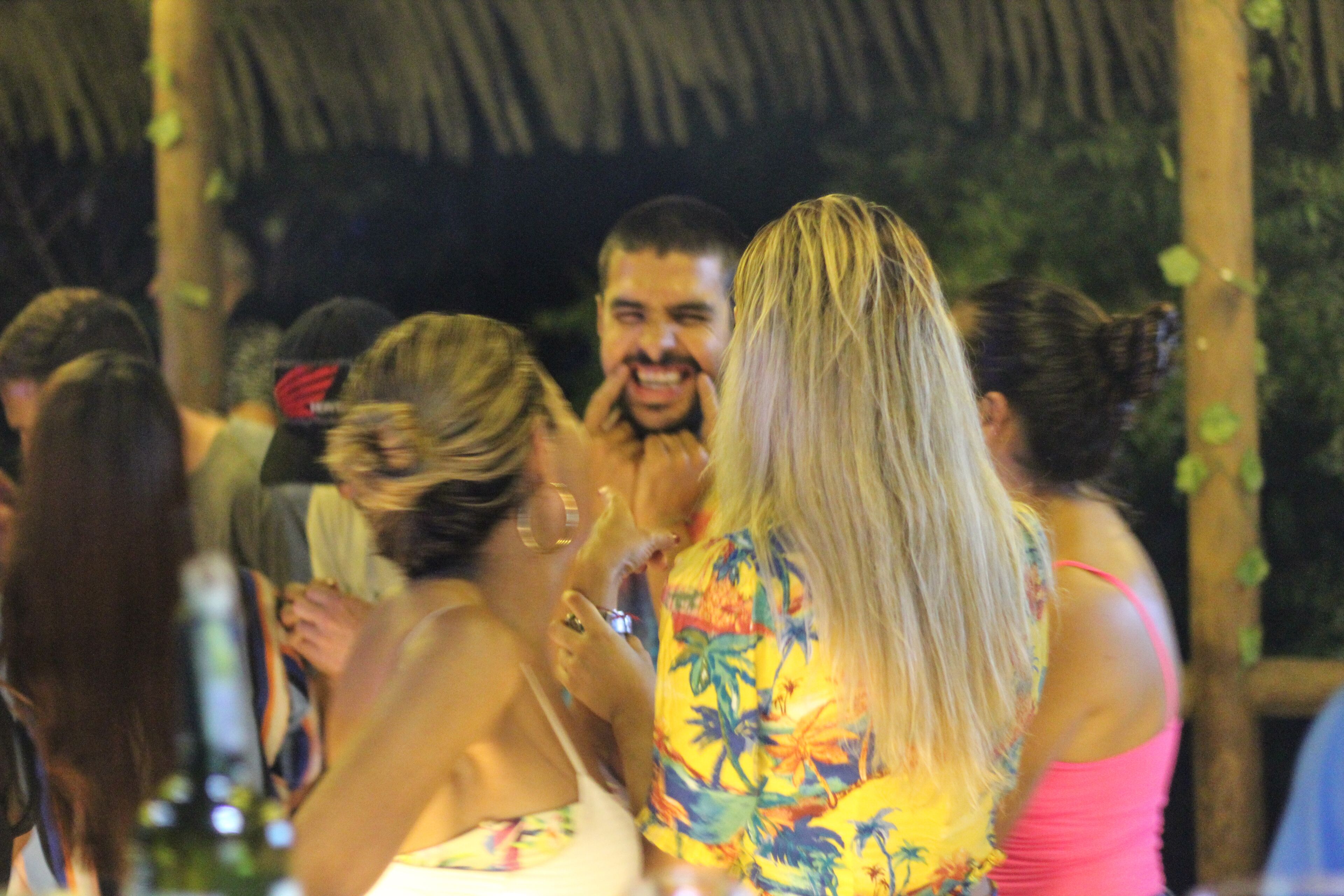 A group of people gathered under a thatched roof structure, possibly at an outdoor event or gathering.