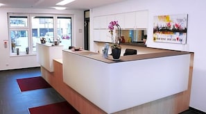 A reception area with a reception desk, a potted plant, and a cityscape painting on the wall.