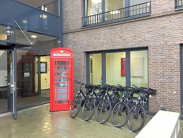 A red telephone booth and a row of bicycles parked outside a building with a brick facade.