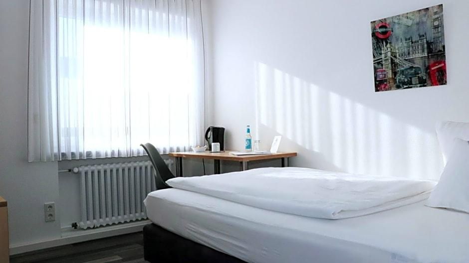 Ein Hotelzimmer mit einem Bett, einem Schreibtisch mit Stuhl, einem Heizkörper und einem Fenster mit Vorhängen.