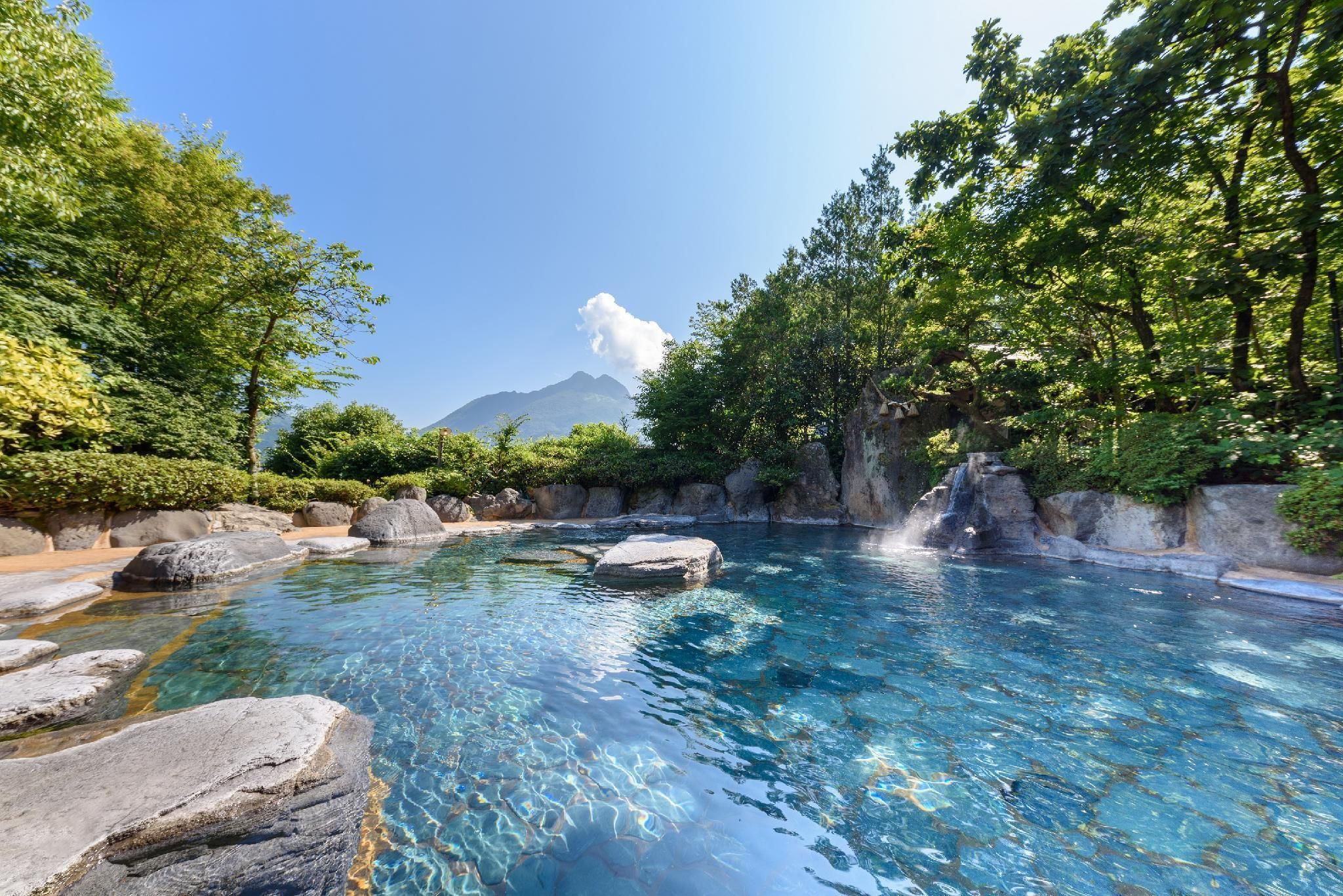 A clear pool surrounded by rocks and lush greenery with a mountain in the background.