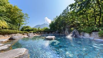 A clear pool surrounded by rocks and lush greenery with a mountain in the background.