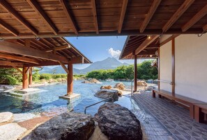 Un onsen japonès tradicional amb estructures de fusta, un camí de pedra i vista a la muntanya.