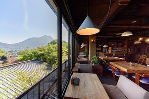 A restaurant with a view of mountains and greenery, featuring wooden tables and chairs, and hanging pendant lights. - Musouen (Yufu)