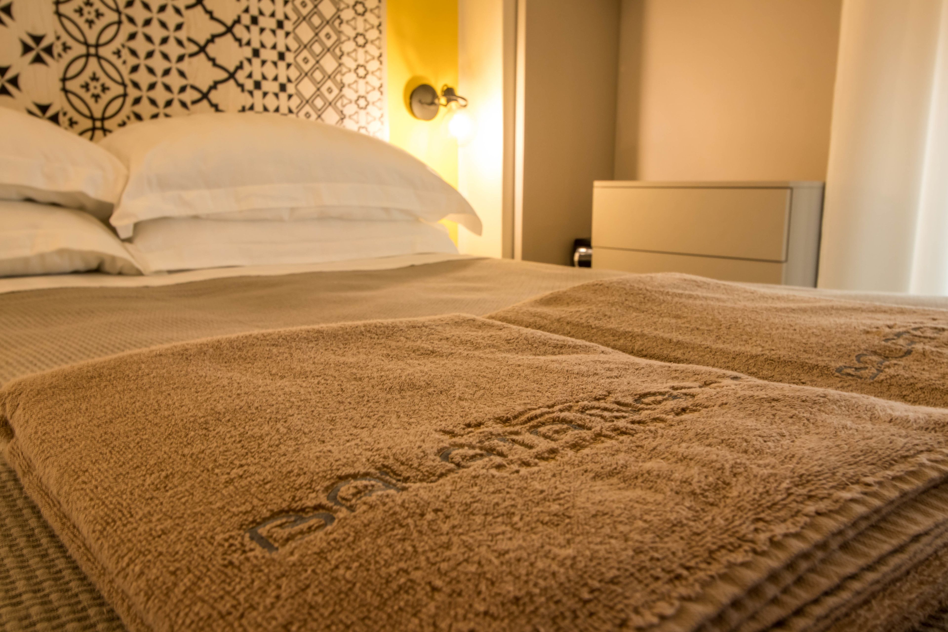 A bed with a beige blanket and pillows, a patterned headboard, and a bedside table with a lamp.