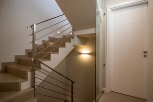 Una escalera moderna con barandilla de vidrio y un elemento decorativo iluminado en la pared.