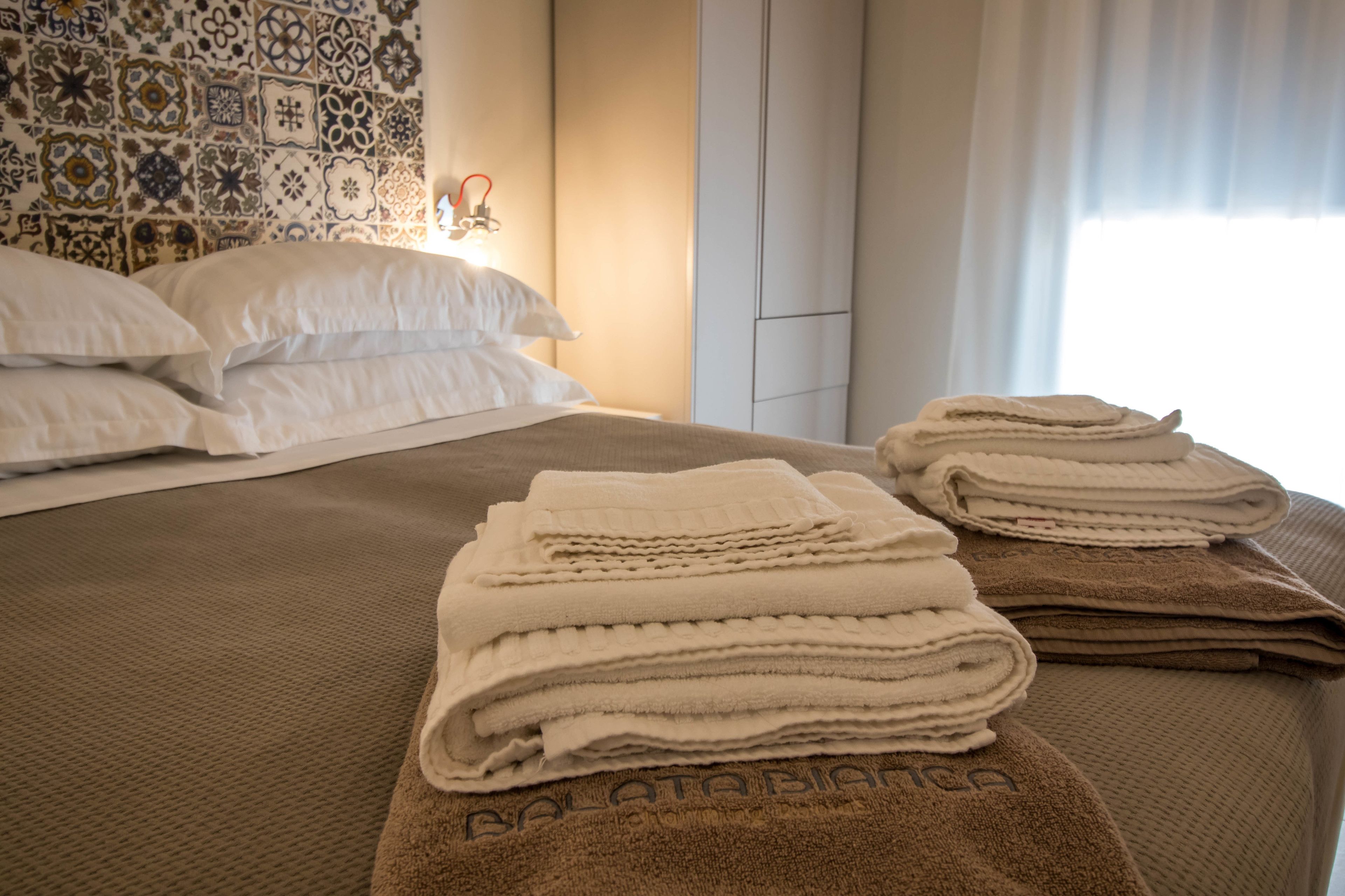 A neatly made bed with white and brown towels, a patterned wall, and a window with curtains.