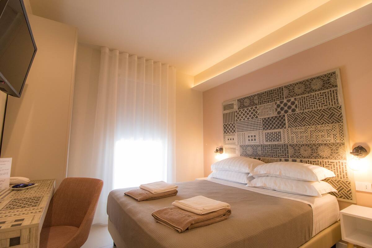 A hotel room with a bed, a chair, a desk, and a TV.