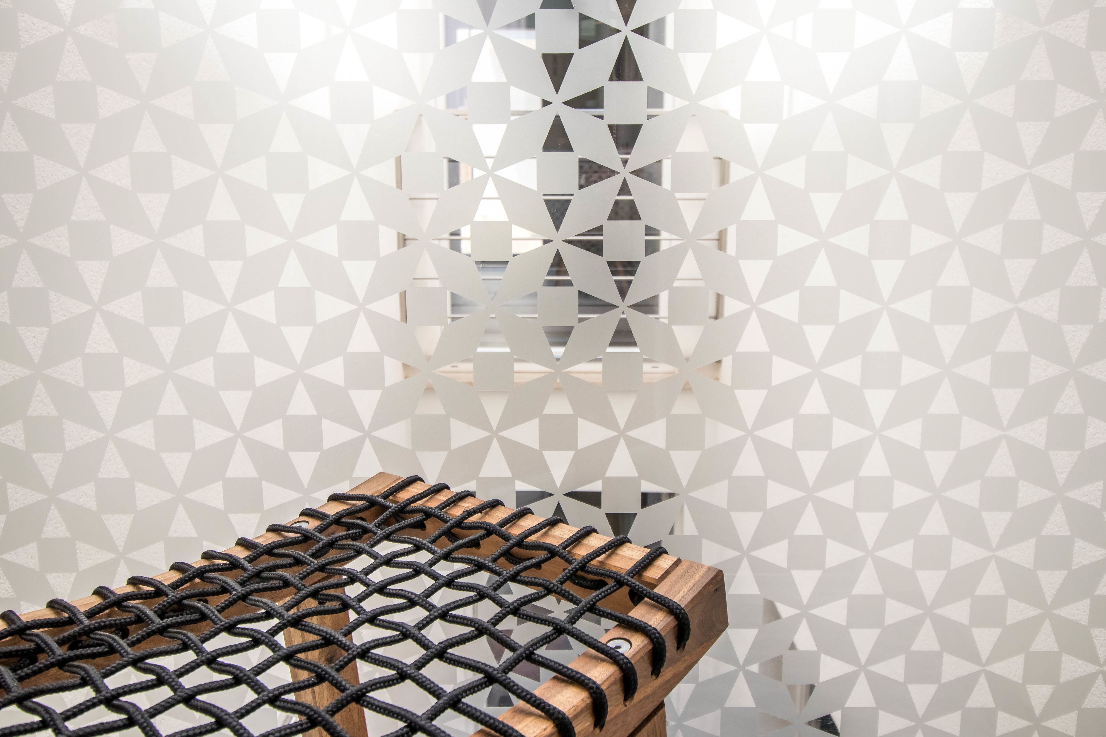A room with a geometric patterned wall, a wooden bench, and a window with a view of buildings.