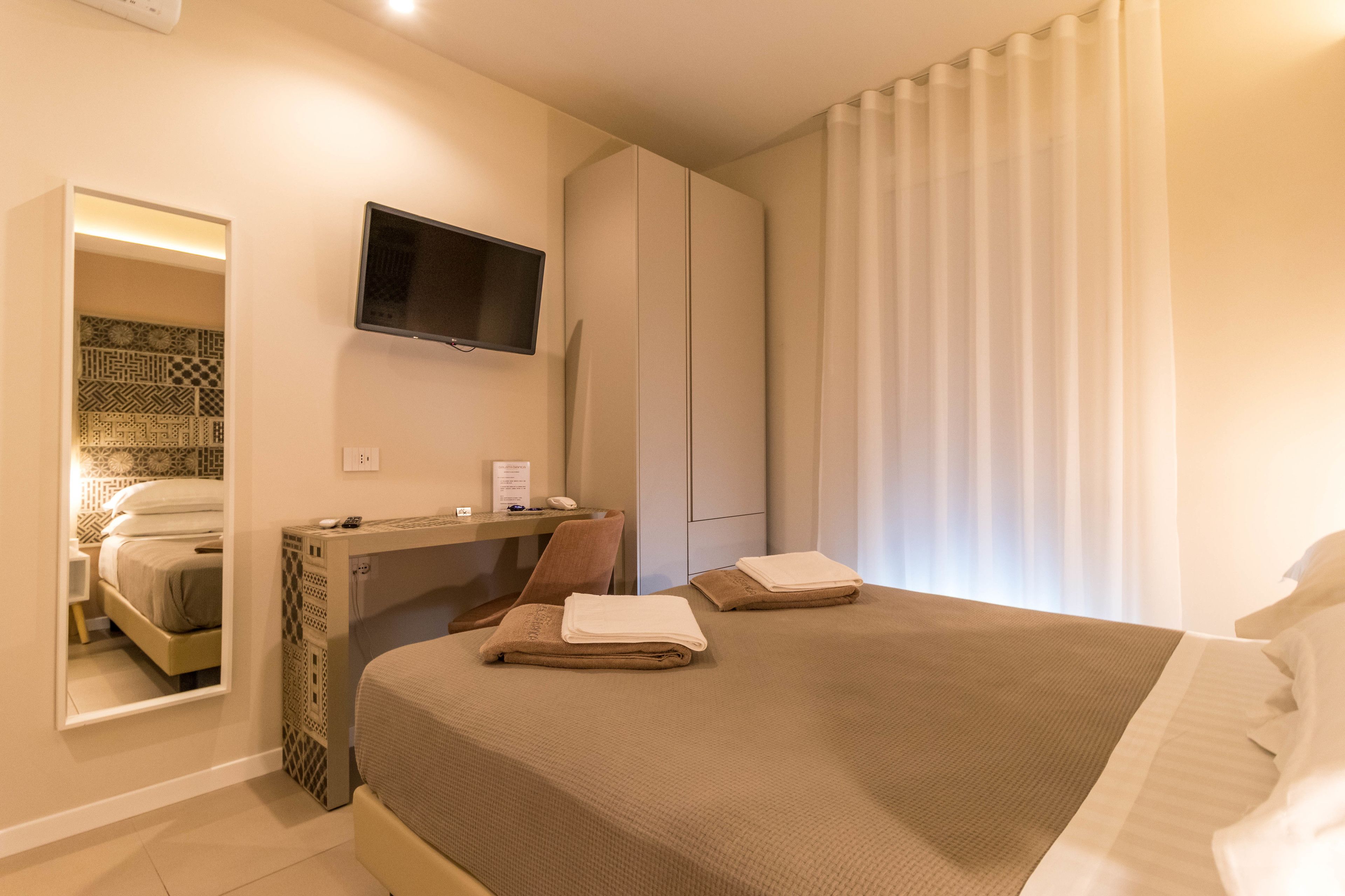 Camera d'albergo con un letto, una scrivania, una sedia, una televisione e una finestra con tende.