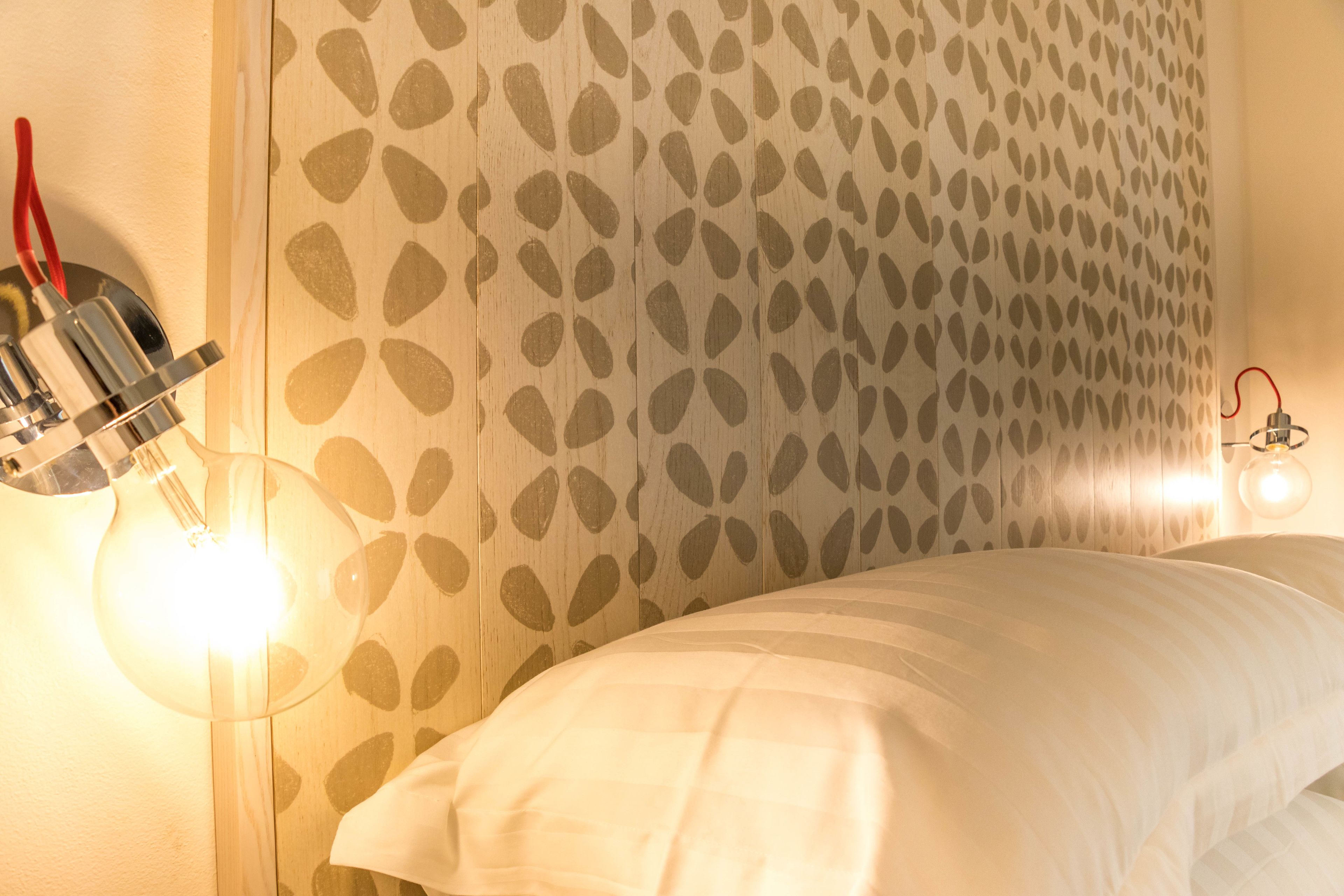 A bedroom with a patterned wall, a bed with white bedding, and two wall-mounted lights.