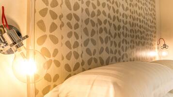 A bedroom with a patterned wall, a bed with white bedding, and two wall-mounted lights.