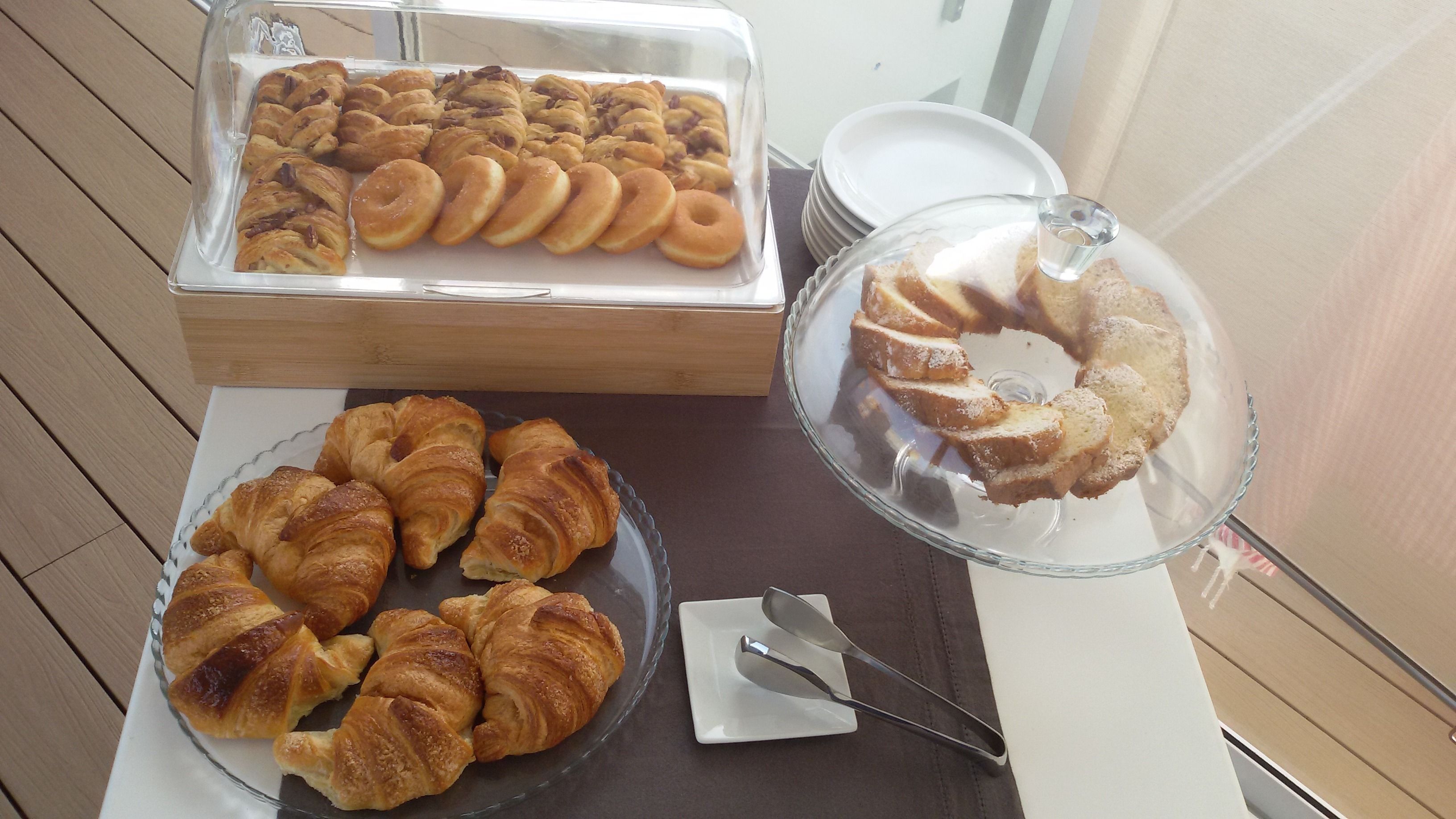 A buffet table with various pastries, including croissants and a cake, and a glass container with a cake slice on a plate.