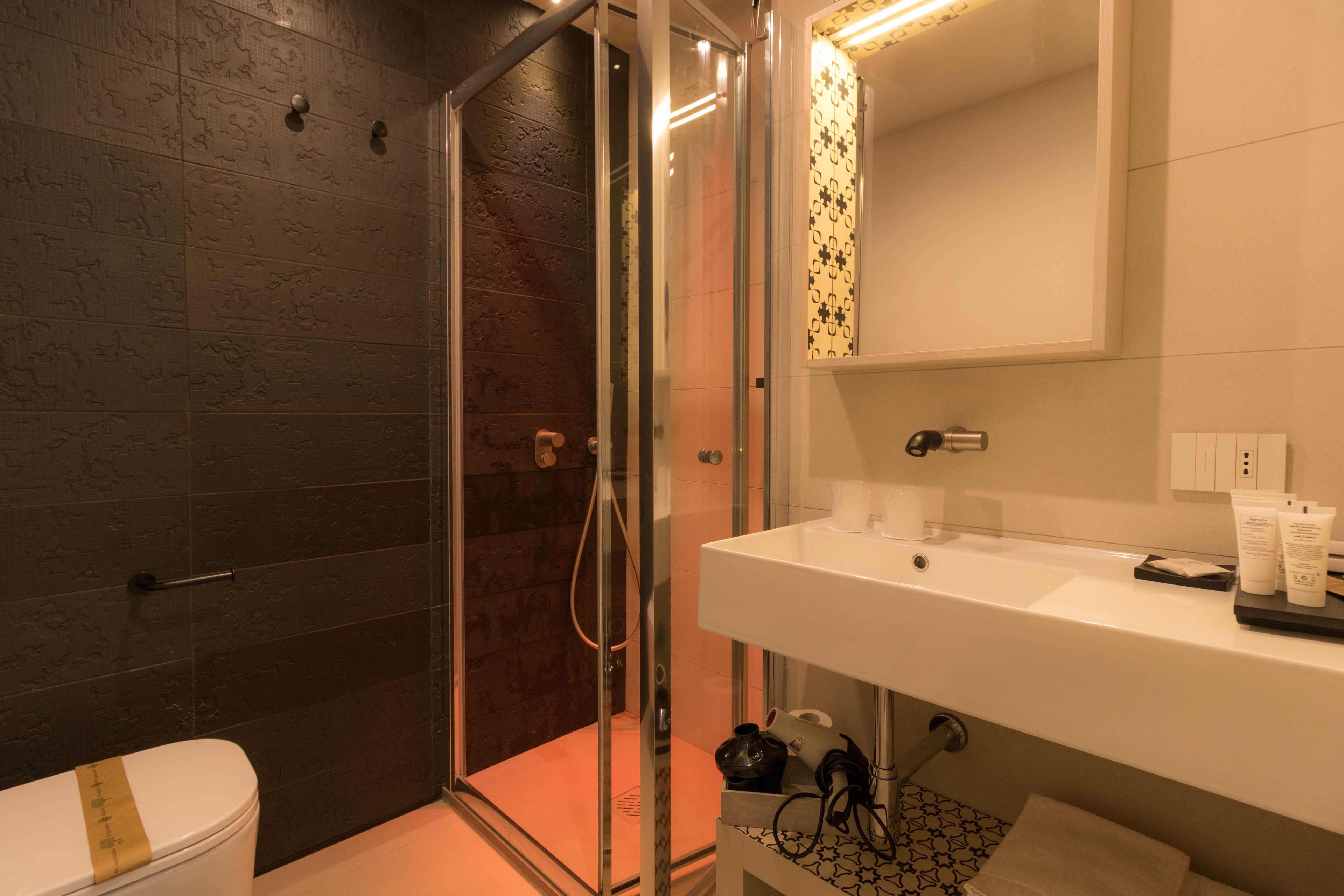 A modern bathroom with a glass-enclosed shower, a white sink with toiletries, and a patterned tile backsplash.