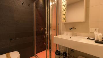 A modern bathroom with a glass-enclosed shower, a white sink with toiletries, and a patterned tile backsplash.