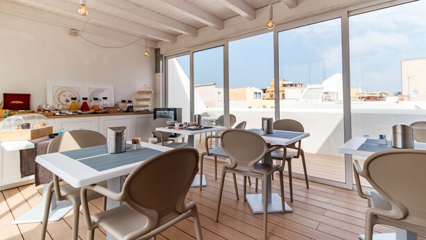A modern dining area with tables and chairs, a kitchen counter, and large windows offering a view of the city.