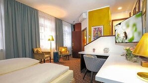 A hotel room with a bed, desk, chairs, and a TV.