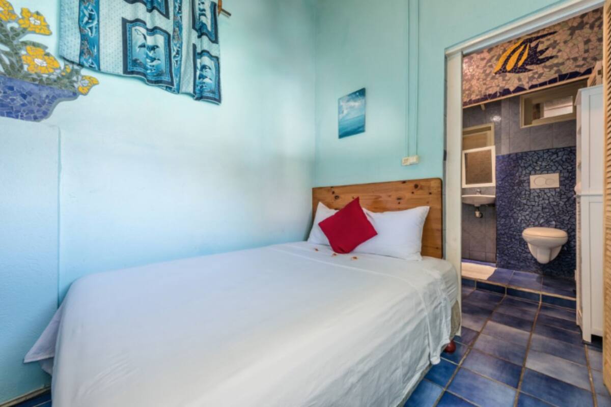 Un dormitorio con cama, cabecera de madera, almohada roja y pared con cuadros.