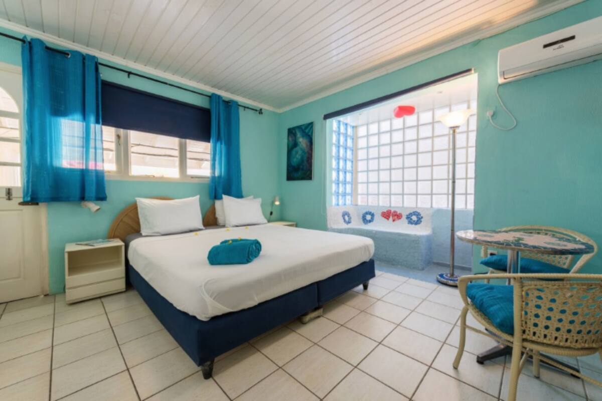 Un dormitorio con cama, mesita de noche, silla, ventana con cortinas y vistas al exterior.