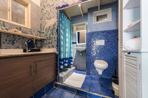 A bathroom with a mosaic tile wall, a sink, a toilet, and a shower area.