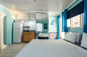 A room with a bed, a small kitchenette, and a bathroom visible through a glass door.