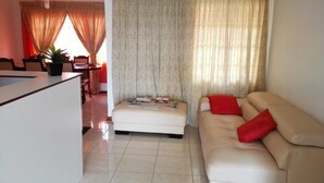 A living room with a sofa, ottoman, and a dining area with a table and chairs. - Rest Shade Bed And Breakfast (Palapye)