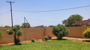 A residential area with a well-maintained lawn, a variety of small trees, and a high wall. - Rest Shade Bed And Breakfast (Palapye)