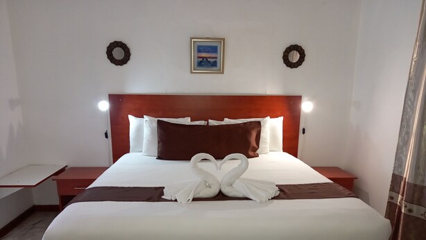 A neatly made bed with white and brown linens, two wall sconces, a framed picture, and two wall-mounted wreaths. - Rest Shade Bed And Breakfast (Palapye)