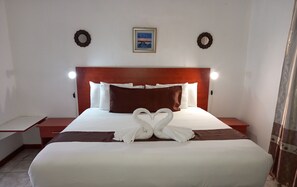 A neatly made bed with white and brown linens, two wall sconces, a framed picture, and two wall-mounted wreaths. - Rest Shade Bed And Breakfast (Palapye)