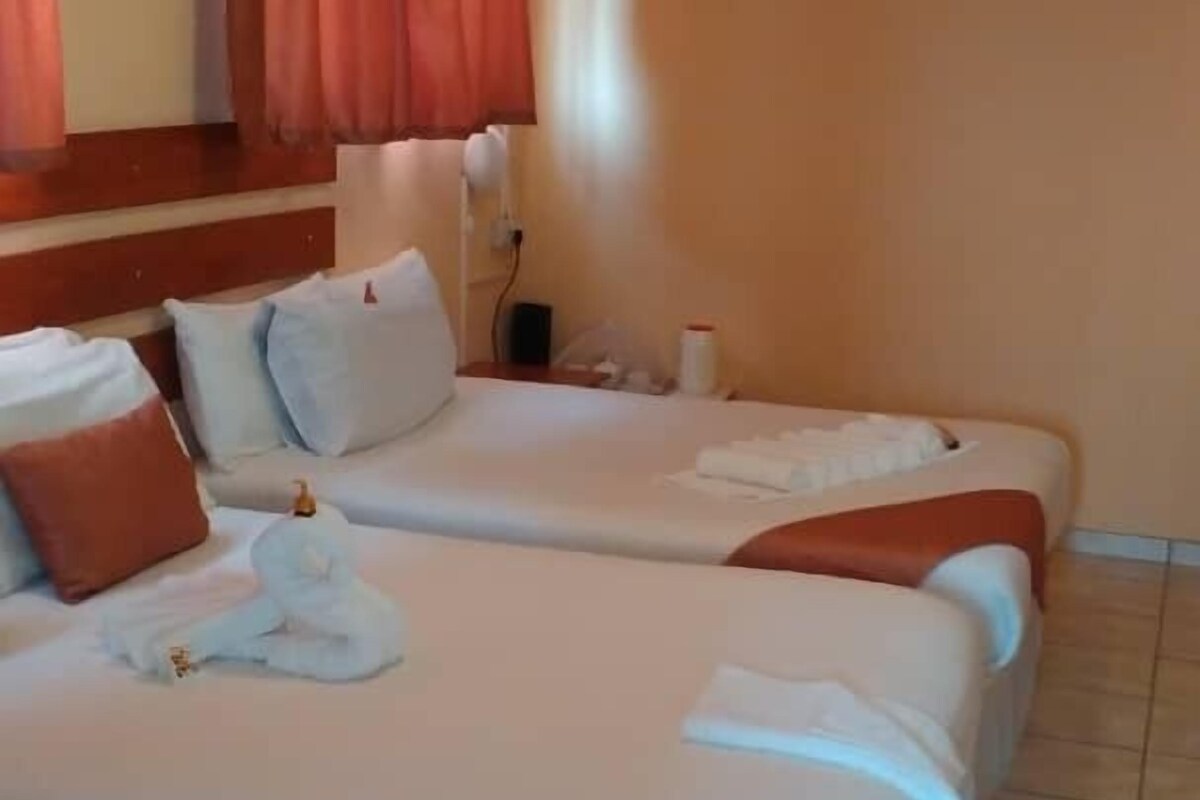 Hotellihuone, jossa on kaksi sänkyä, pieni pöytä ja seinälle asennettu ilmastointilaite.
