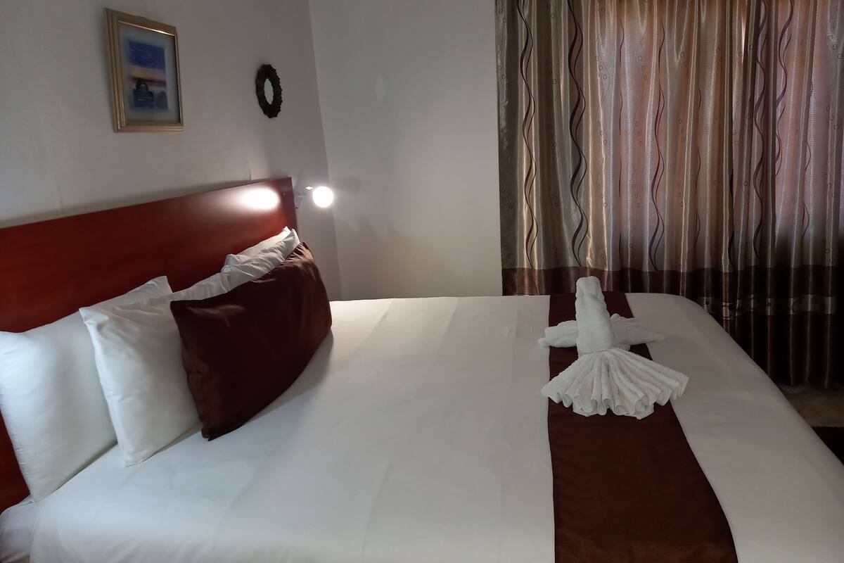 A neatly made bed with white and brown linens, a red headboard, and a framed picture on the wall.
