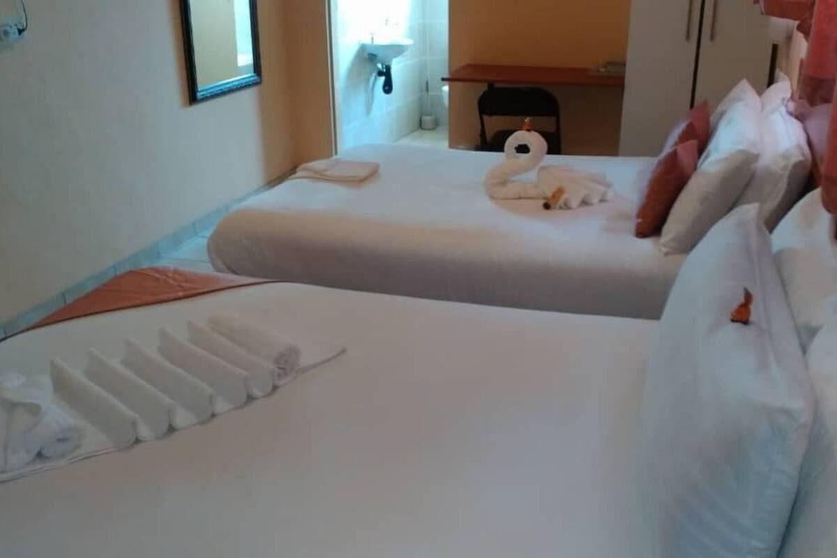 A hotel room with two beds, a bathroom visible through an open door, and a small table with a chair.