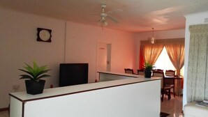A living room with a white sofa, a TV, a ceiling fan, a dining table with chairs, and two potted plants. - Rest Shade Bed And Breakfast (Palapye)