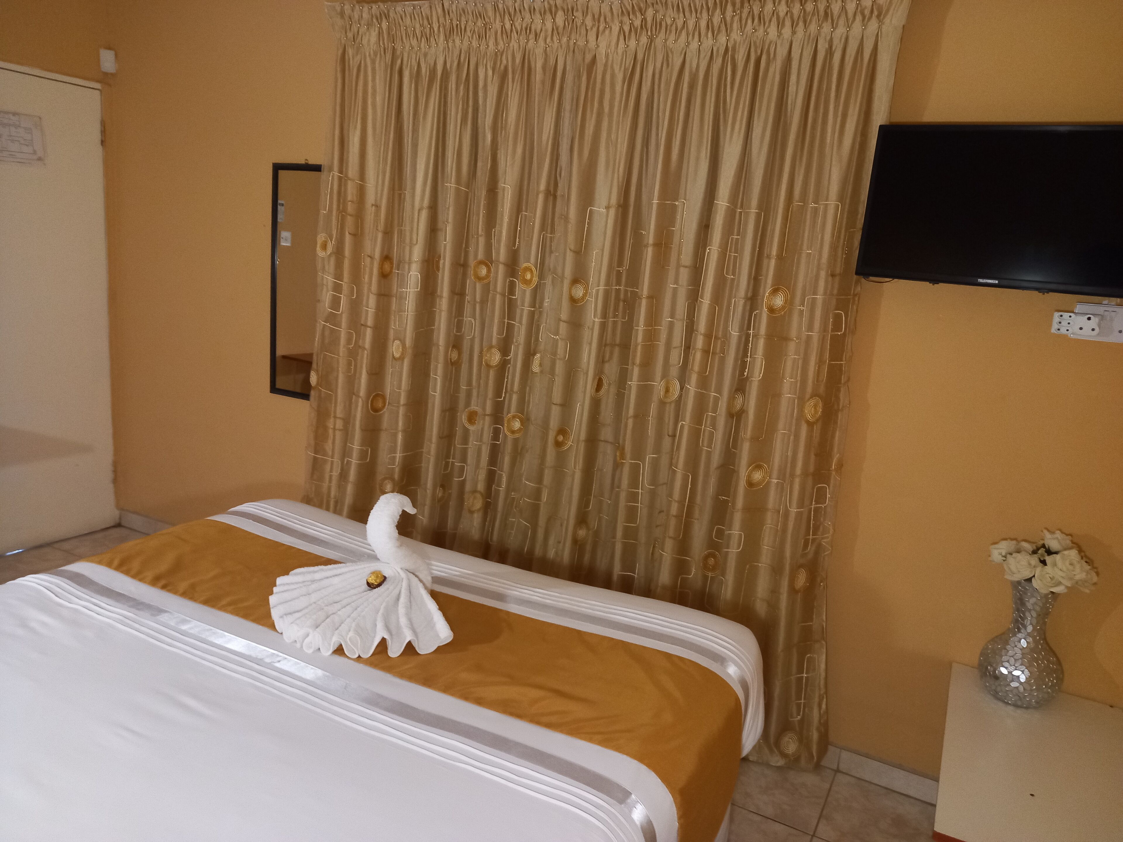 A hotel room with a bed, a television mounted on the wall, and a vase with flowers on a side table.
